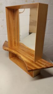 A mirror frame made of Ash with a shelf made of Zebrawood. The shelf is actually inset into the frame and the sides of the frame are beveled to create a depth.
